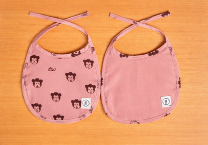 Two pink bibs with monkey pattern on a wooden surface