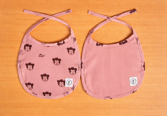 Two pink bibs with monkey pattern on a wooden surface